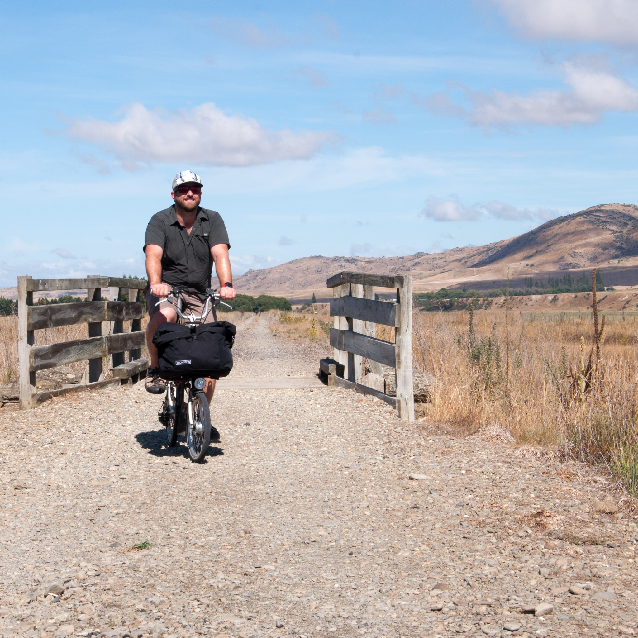 Ben rides through a wooden gate towards the camera with a smile, blue skies behind.