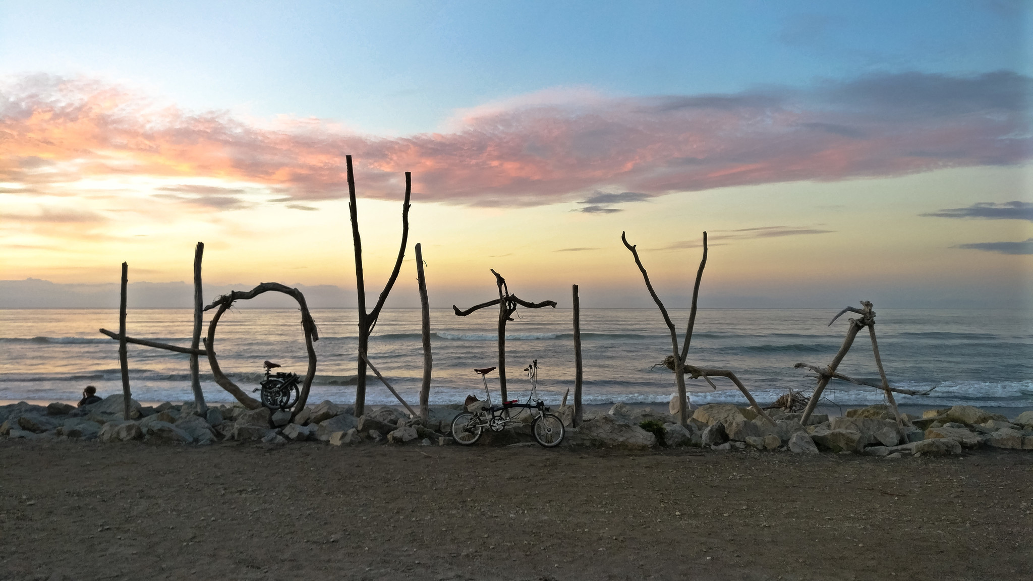 Large branches spell "Hokitika" on a beach facing the water.