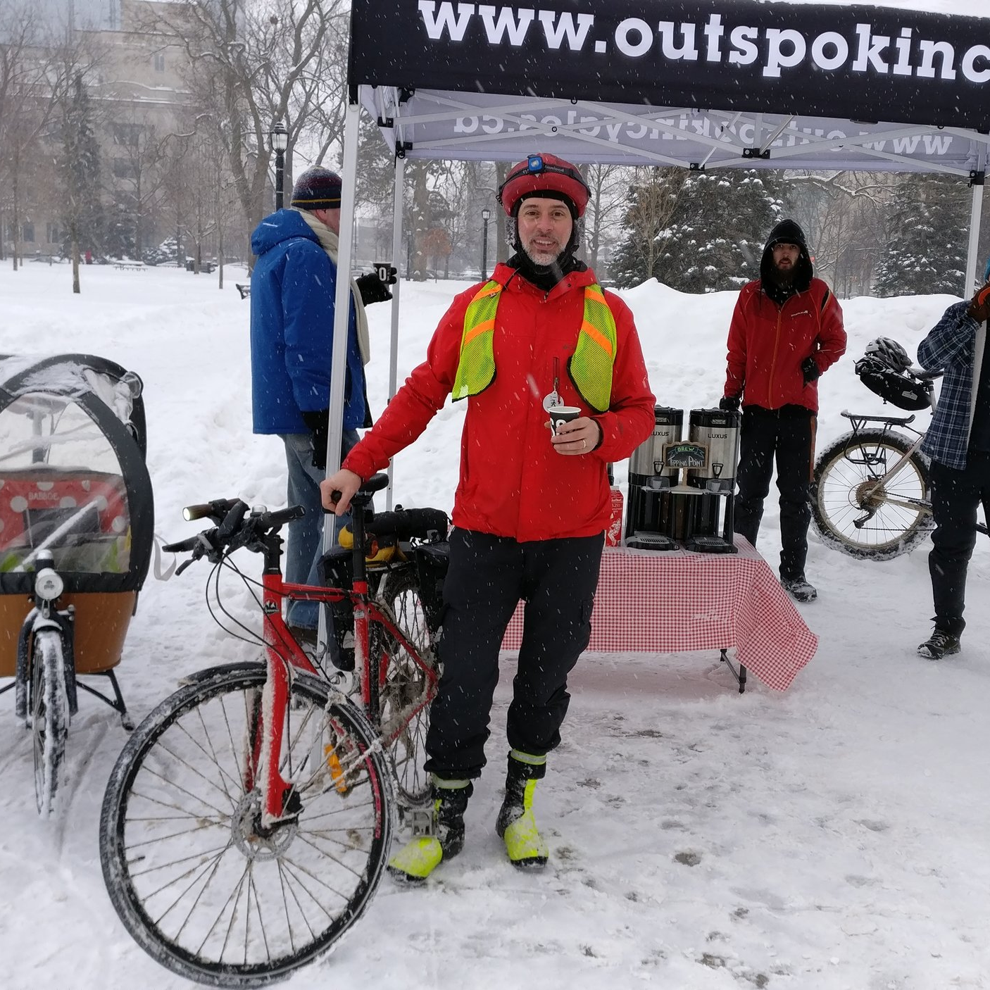 A winter clad cyclist smiles at the camera in front of the coffee station.