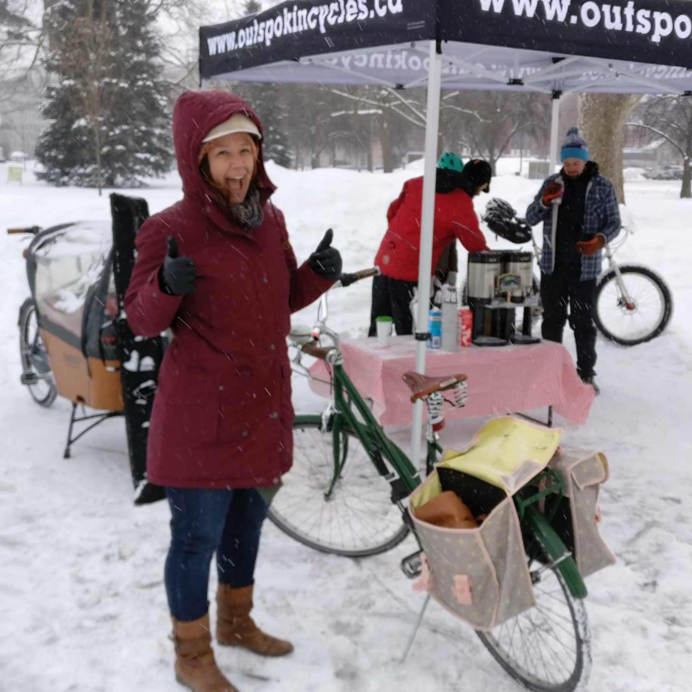 Another winter clad cyclist enjoys a coffee next to her bike.