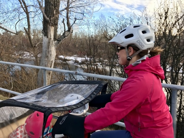 A woman cycles on a box bike with a rain cover and smiles