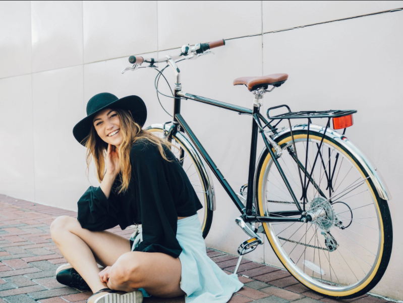 A woman wearing a hat sits relaxed in front of her roadster style bike.