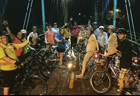 A group of cyclists celebrate a group ride at night.