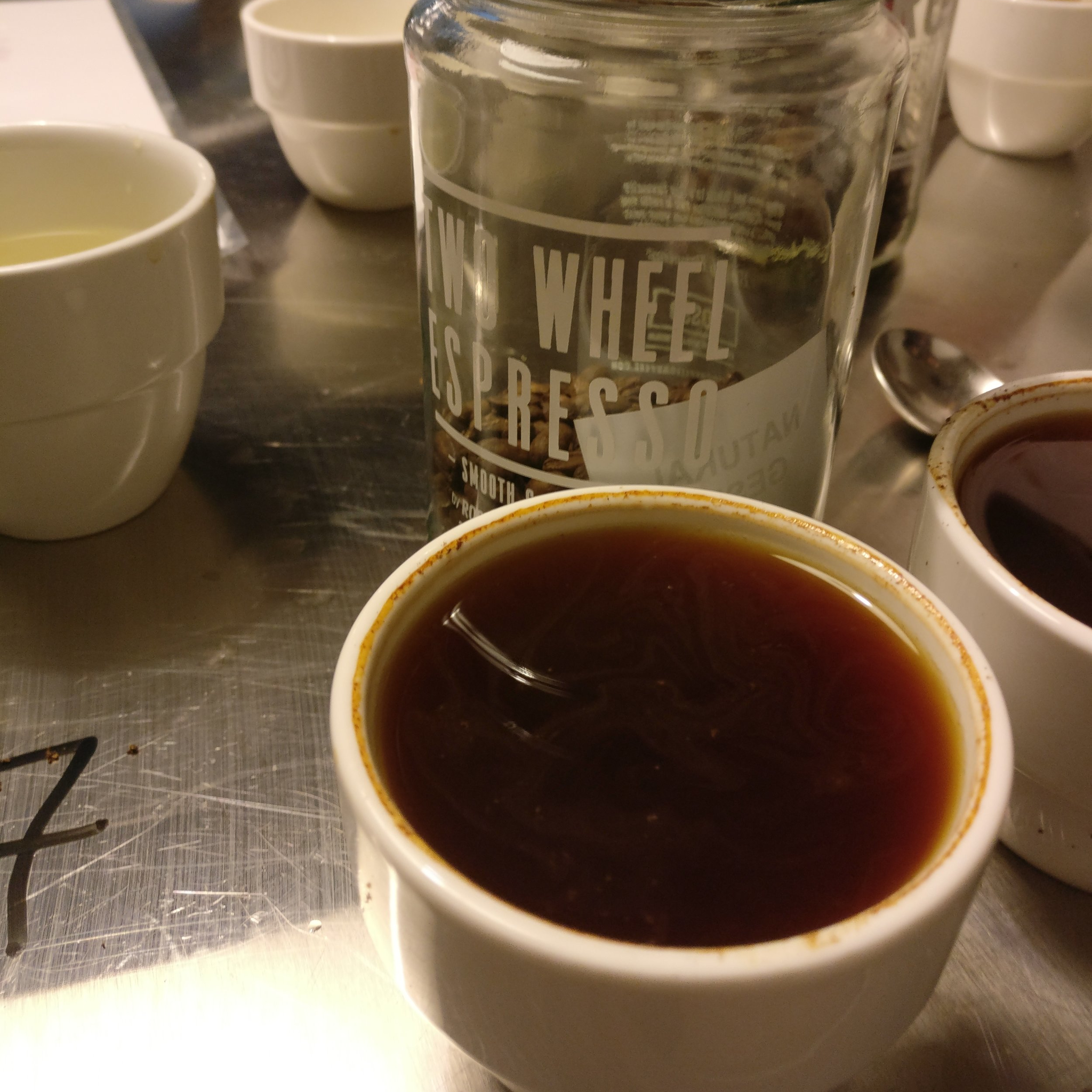 Close up of a fresh cup of coffee, the Rosso bean jar behind.