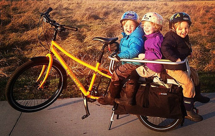 Three small children grin from the back of the Xtracycle longtail bike.