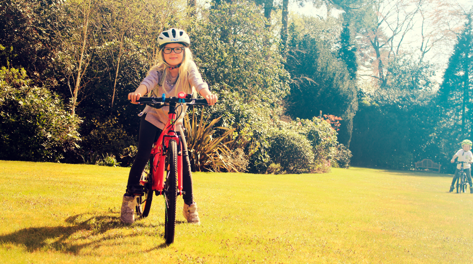 A girl riding her bike on the grass smiles at the camera