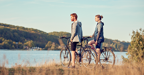 A woman and a man with their bikes look out of frame in a field.