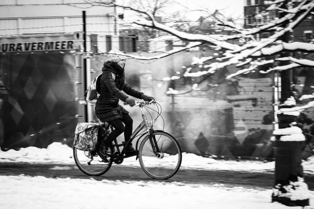 A woman dressed for winter rides her bike on a snowy urban road.