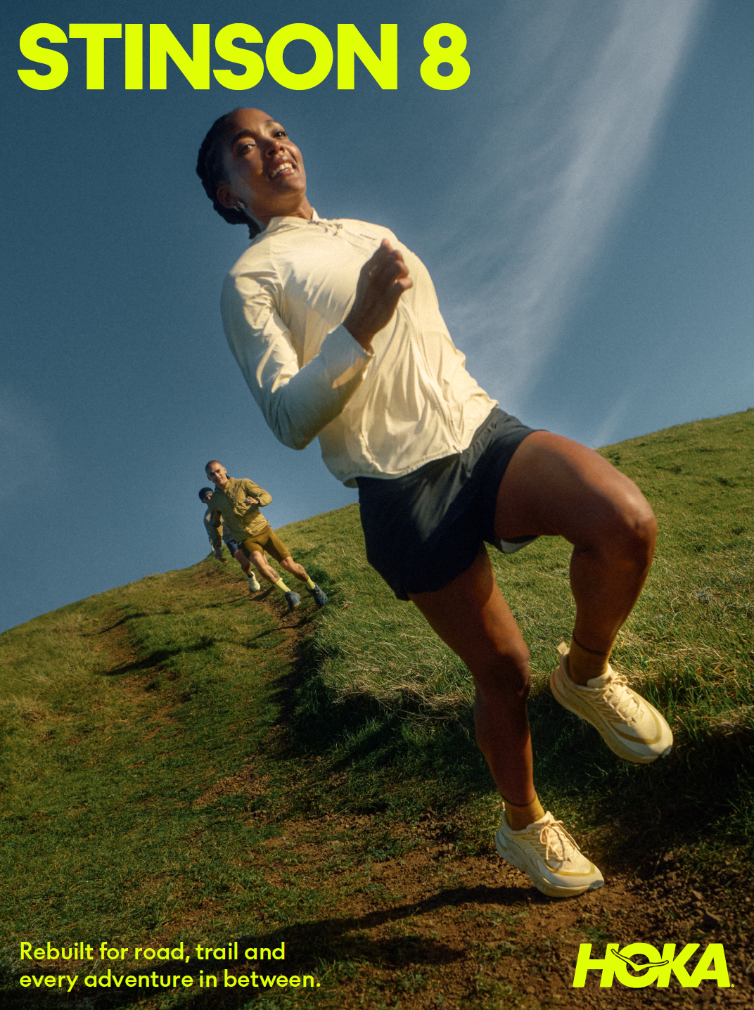 Runners moving across a grassy hillside in the HOKA Stinson 8