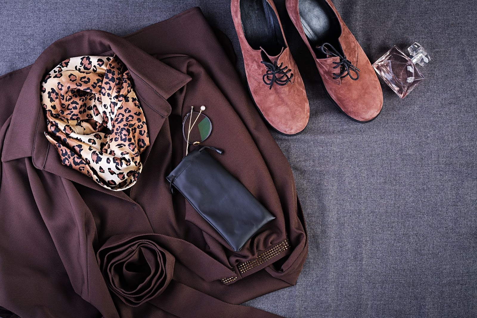 A set of women's clothing consisting of brown footwear, perfume, a brown leopard pattern scarf, a pair of brown suits, and sunglasses.