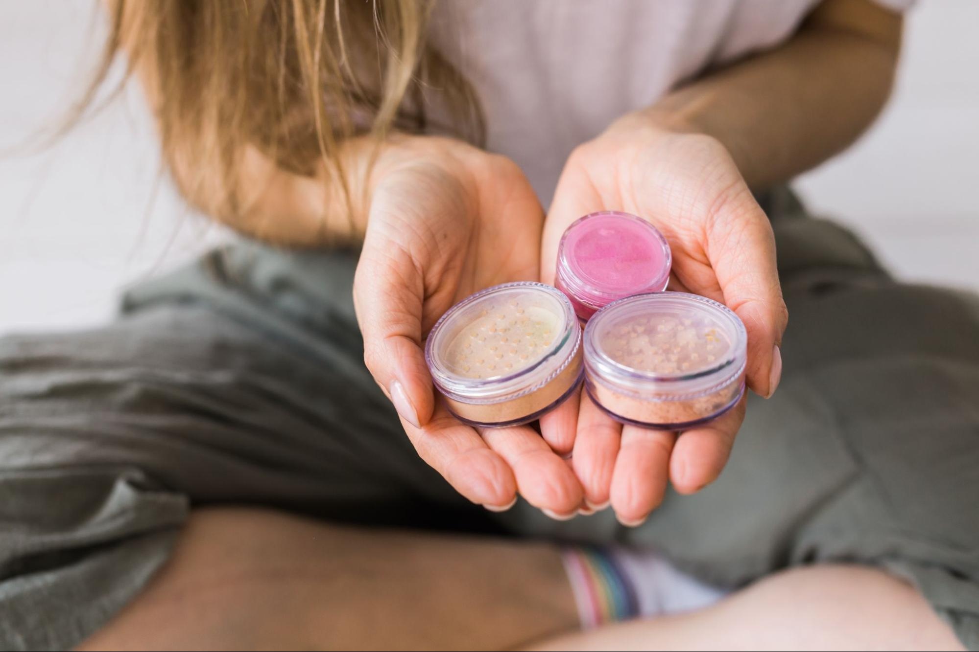 Woman holding containers of makeup and lip scrub. 