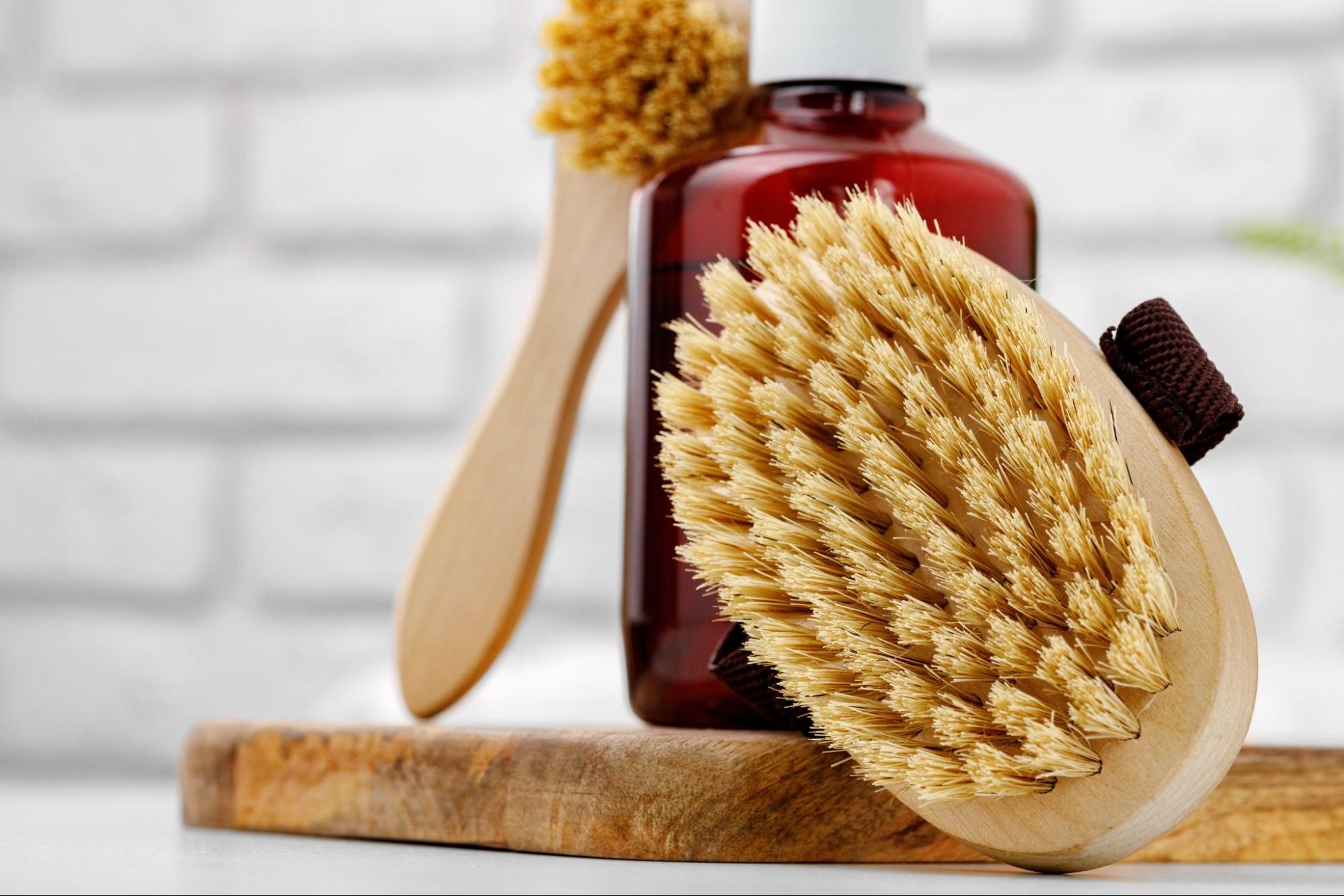Two body massaging brushes resting against a red bottle.