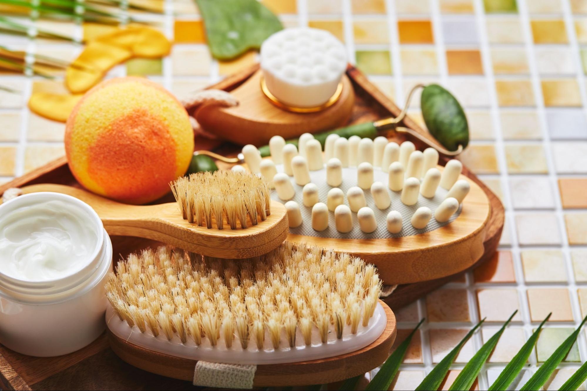 Three dry brushes sitting near some body creams and a round-shaped sponge.