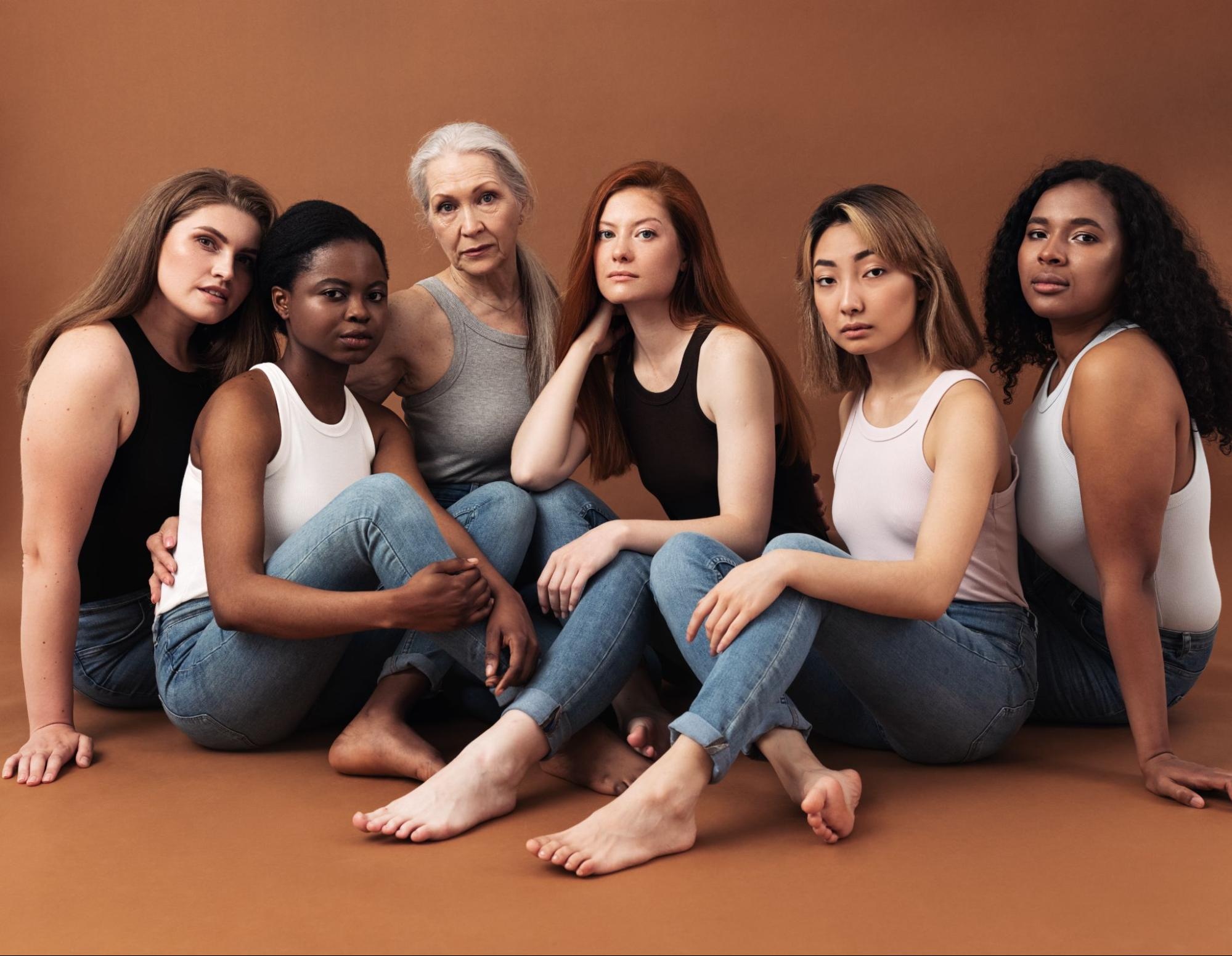 A group of women wearing tank tops sit and pose for their picture.