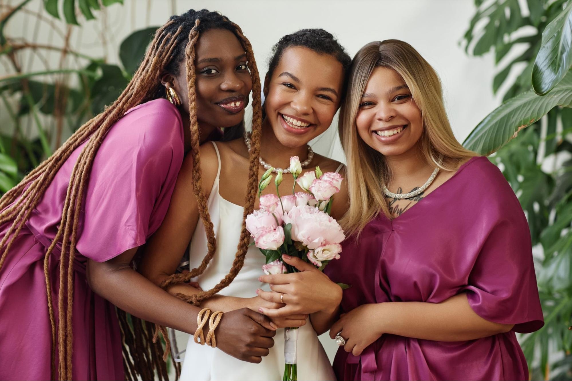 Two bridesmaids dressed in matching pink dresses pose with the bride for a picture.