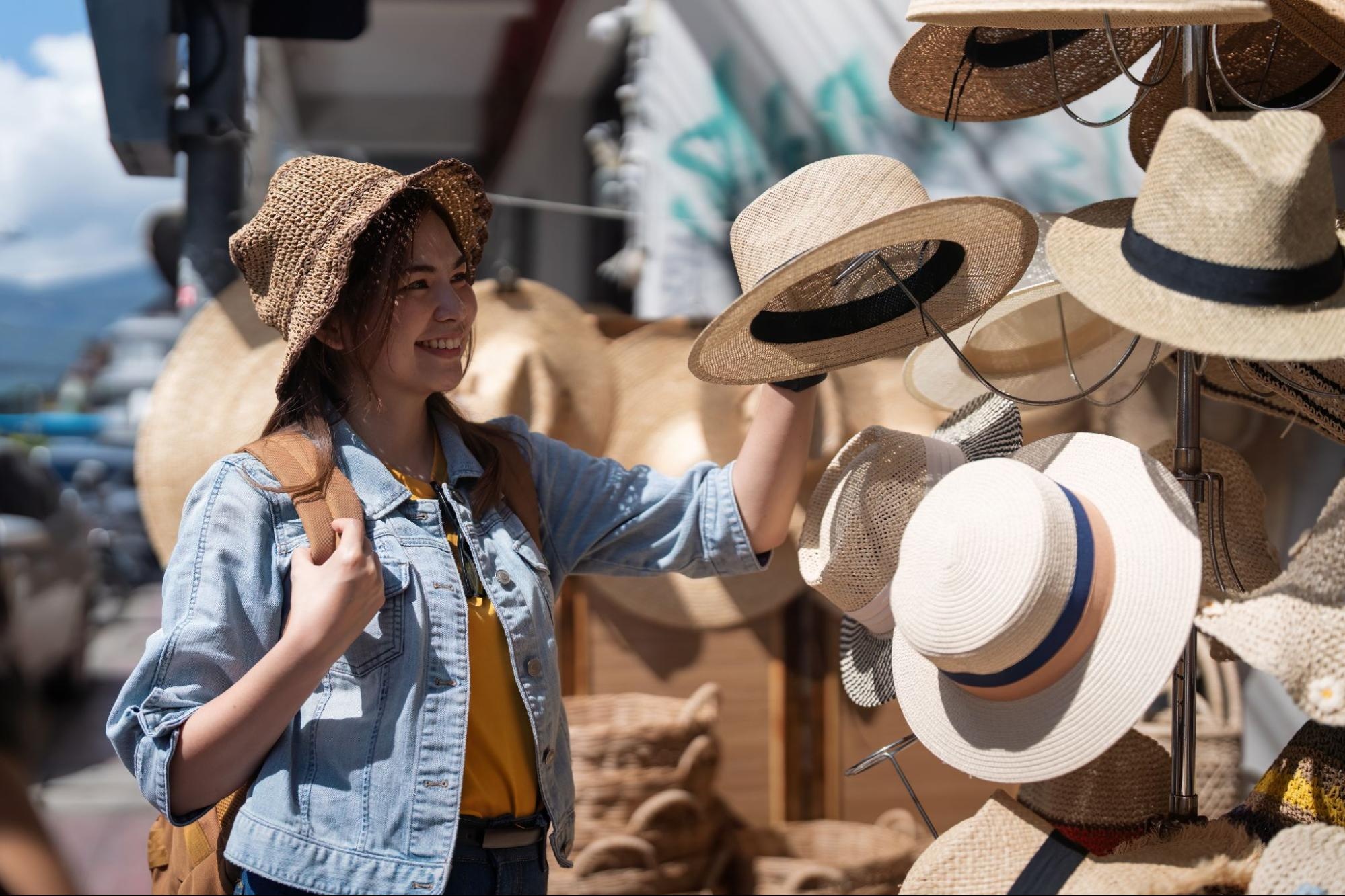 A young woman shops for sunhats of various styles.
