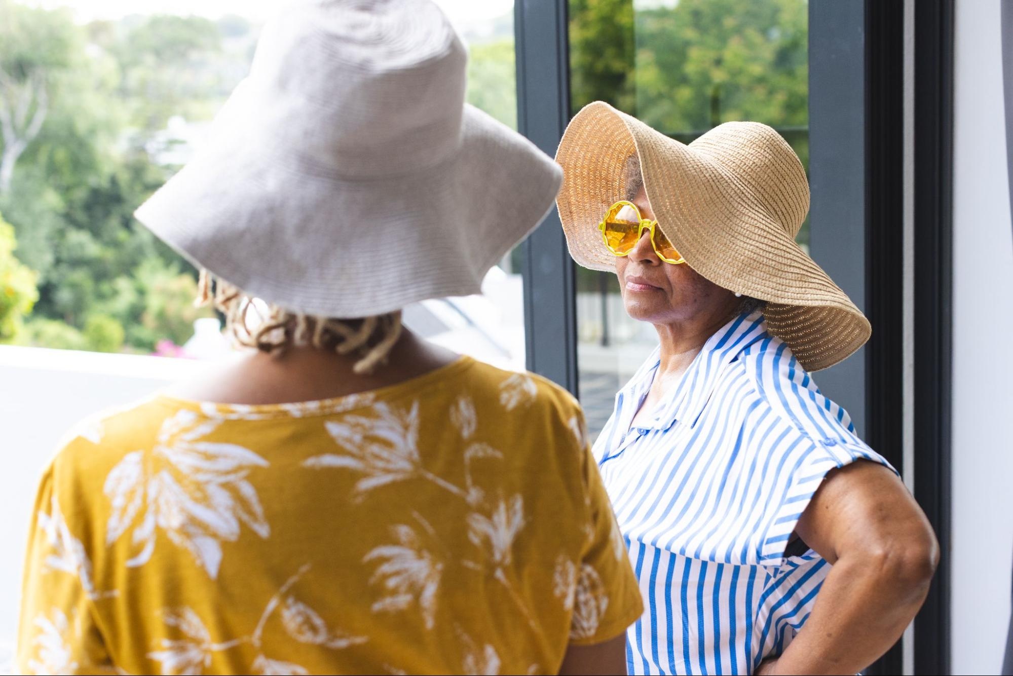 Two women have a conversation while wearing sun hats.