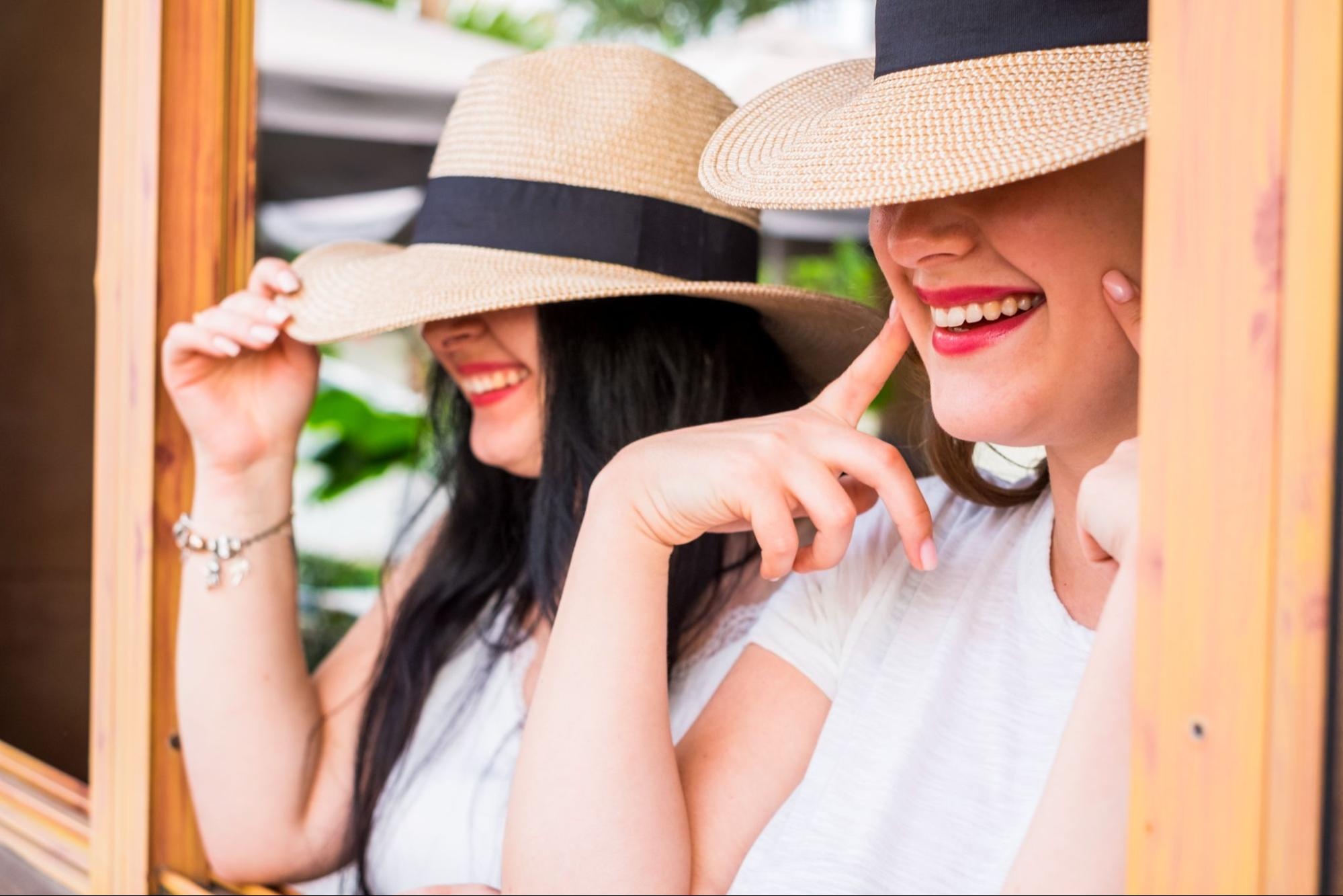 Two women flash smiles while wearing enlarged sun protective hats.