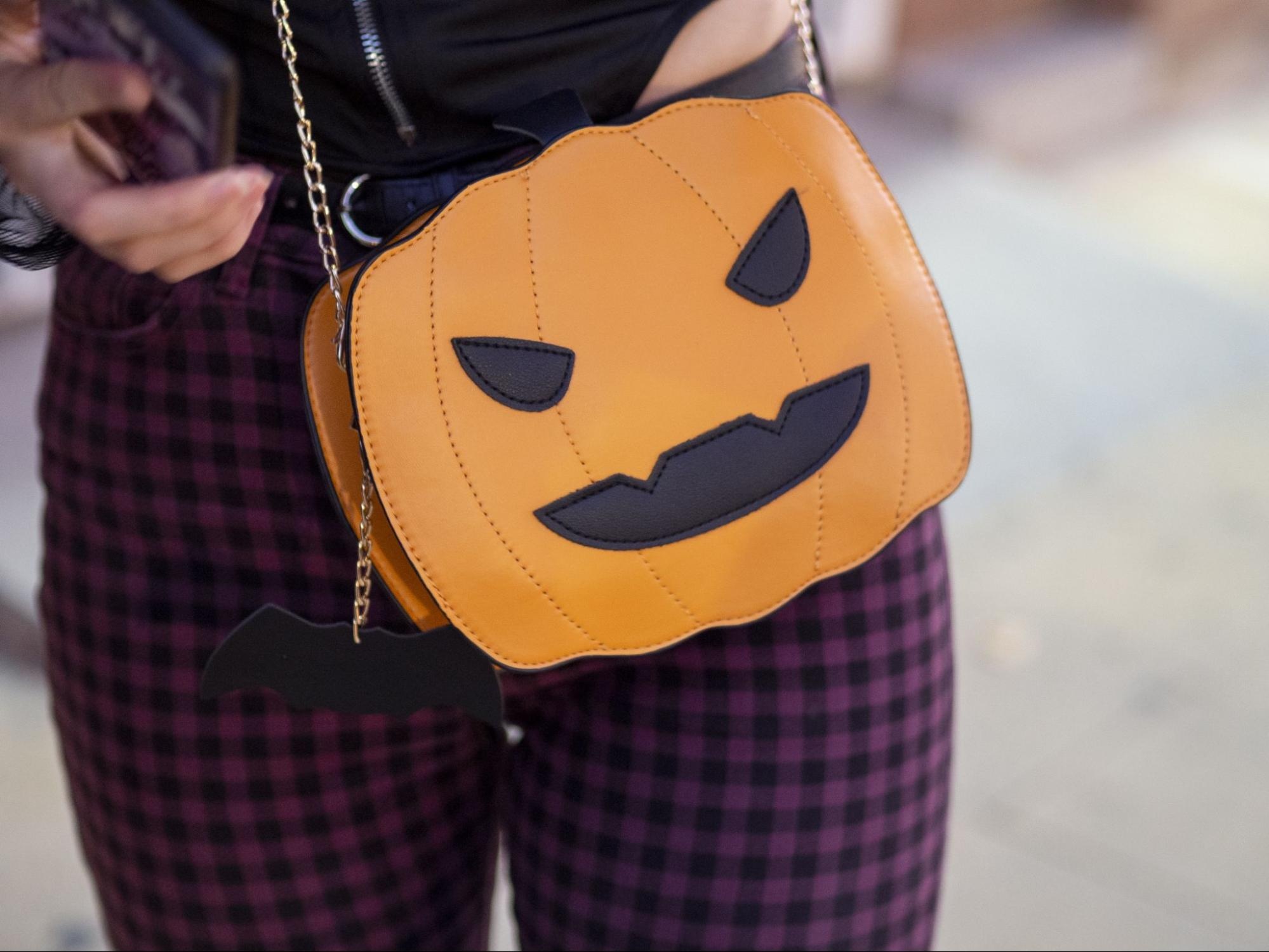 a woman is holding a purse with a pumpkin face on it