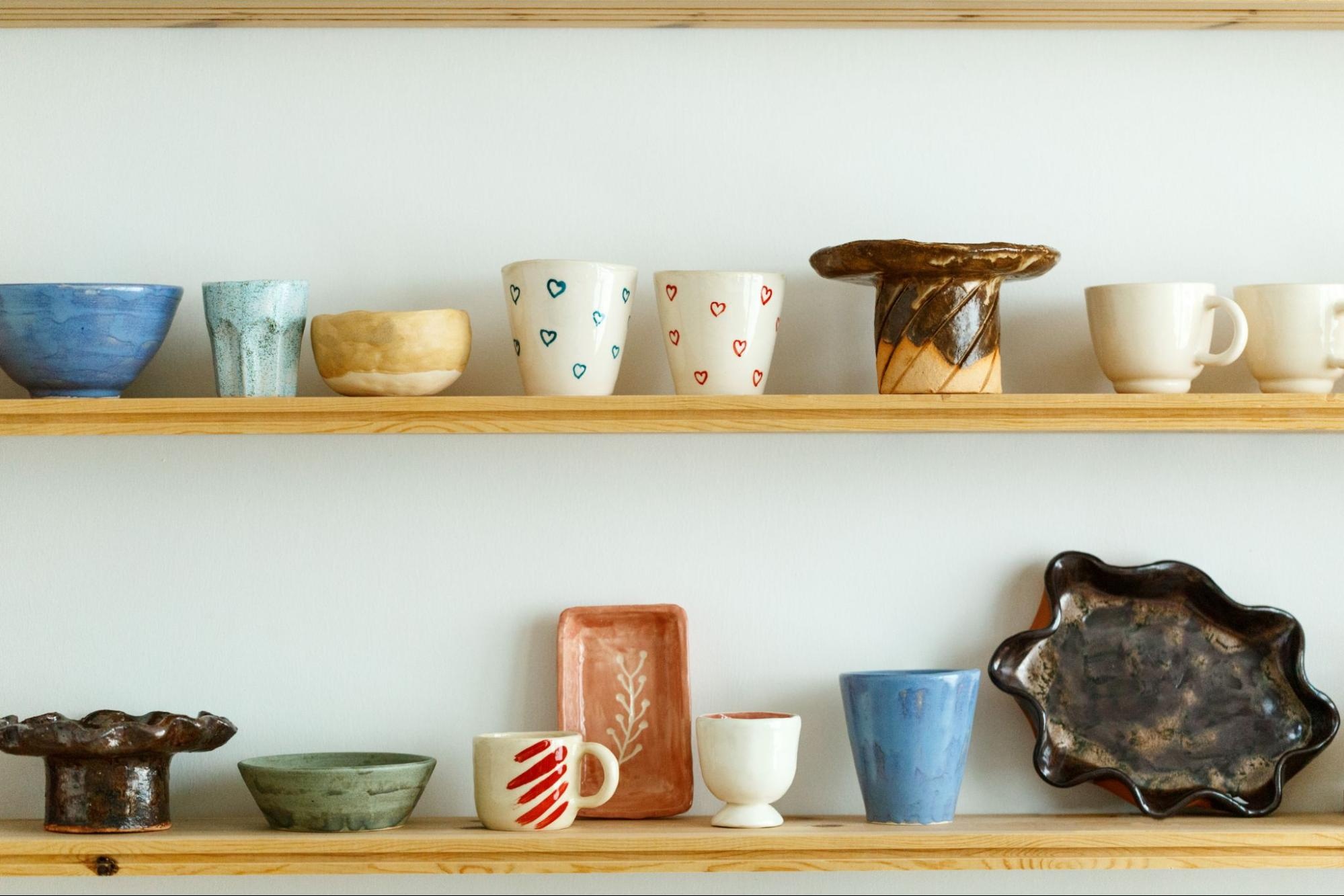 Coffee mugs displayed alongside other handmade ceramic pottery on shelves, arranged creatively for a stylish and artisanal presentation.