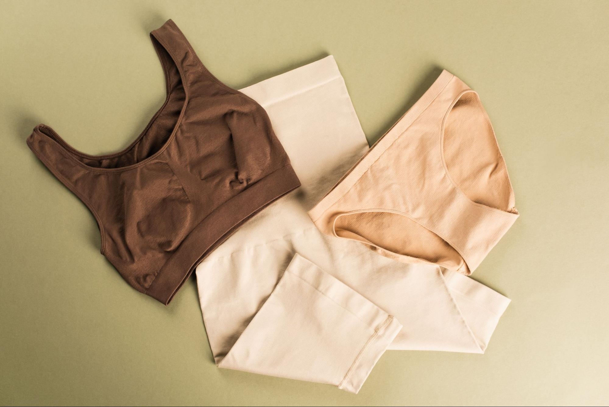 A top view of three cotton shapewear pieces in brown and nude tones, laid flat on a beige background.A top view of three cotton shapewear pieces in brown and nude tones, laid flat on a beige background.