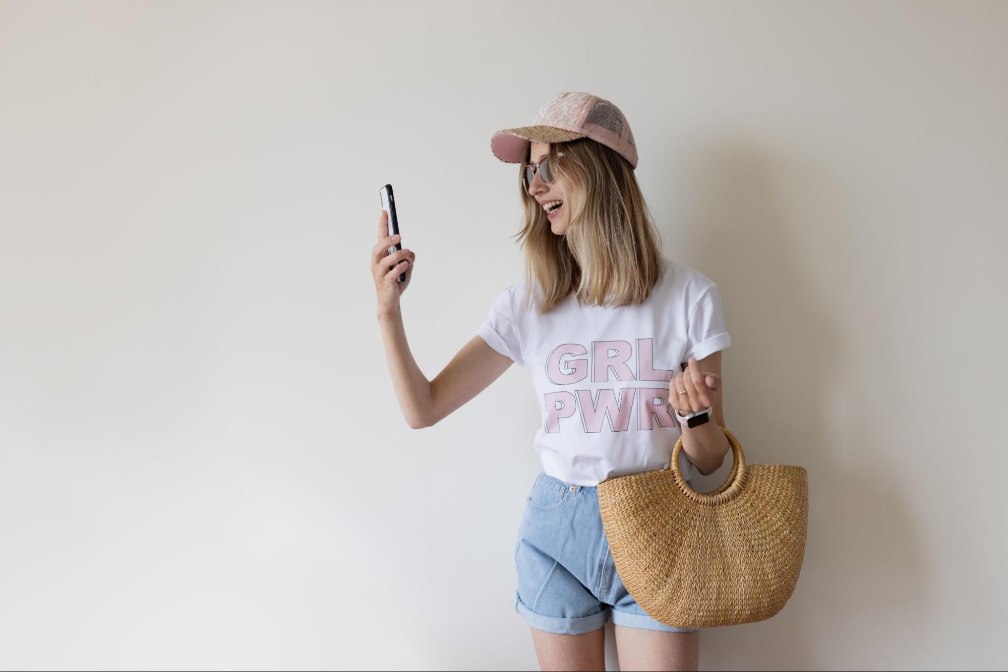 Woman wearing a hat and holding a purse taking a photo of herself. 