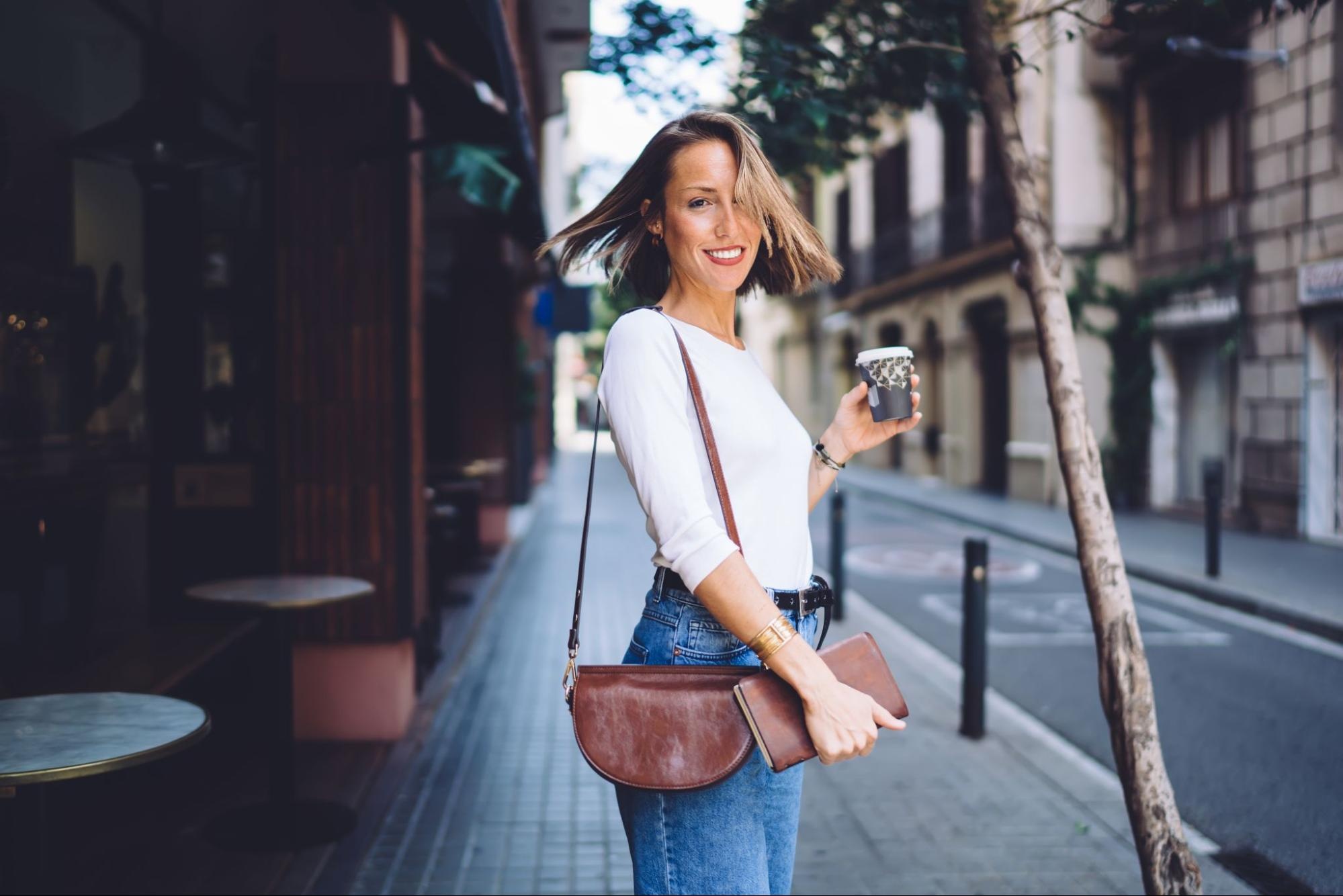 A stolen shot of a woman carrying a shoulder bag while holding a cup of coffee.