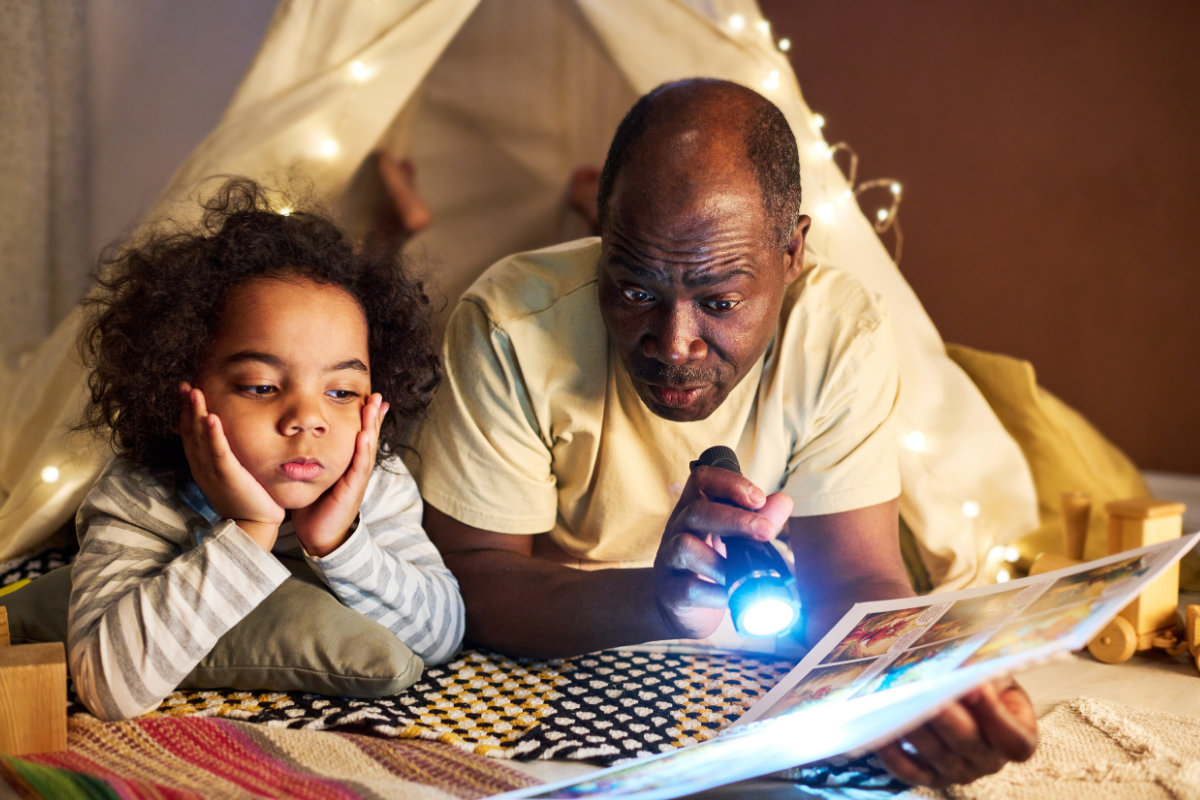 man and child looking at book with flashlight
