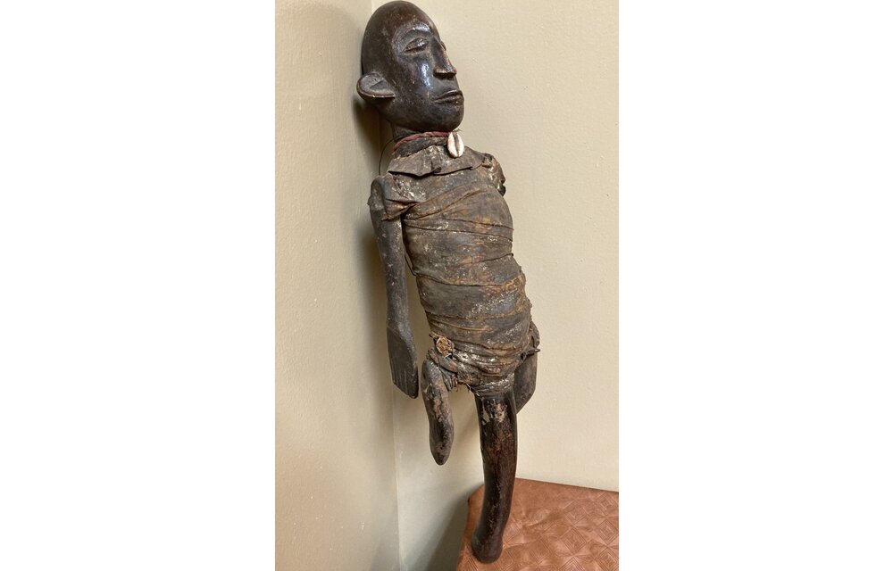 Makonde figure with handle. The Makonde live in East Africa in Mozambique, Tanzania with a small group in Kenya. This figure is used by entertainers and storytellers. Wood with cotton fabric and a cow