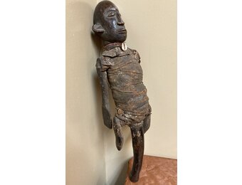 Makonde figure with handle. The Makonde live in East Africa in Mozambique, Tanzania with a small group in Kenya. This figure is used by entertainers and storytellers. Wood with cotton fabric and a cow