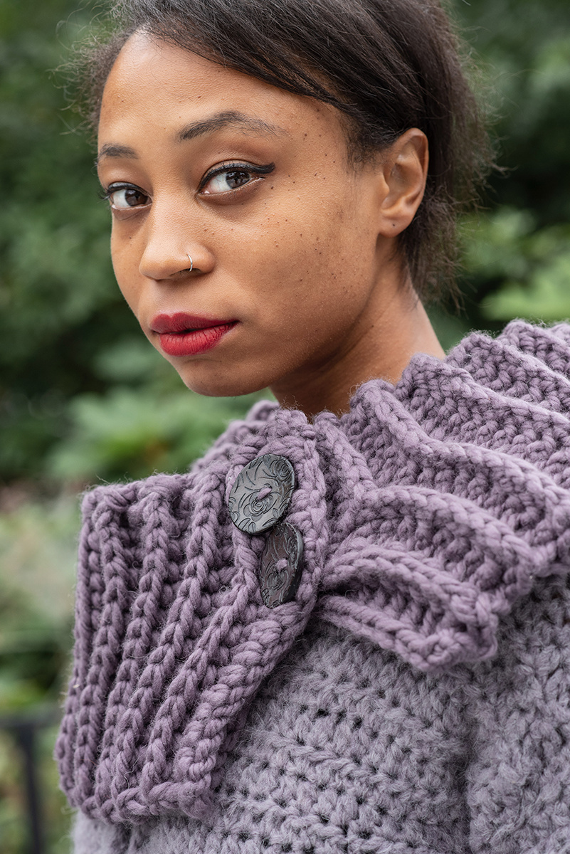 A Black woman stares intensely at the camera. She is wearing a lavender ribbed chunky crocheted collar.