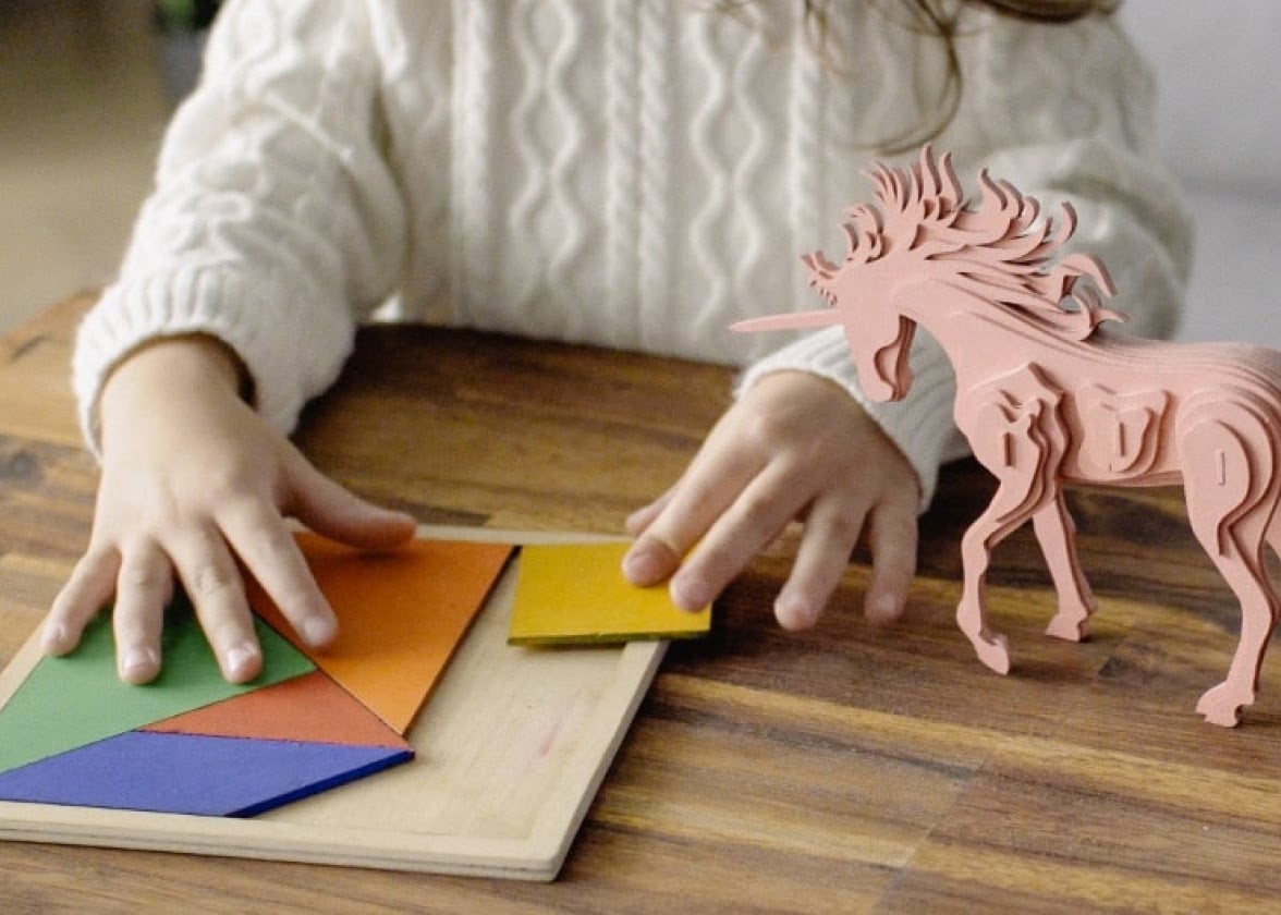 Hands of a child solving a tangram and a 3D horse on the side, both lasercut by FLUX Beamo.