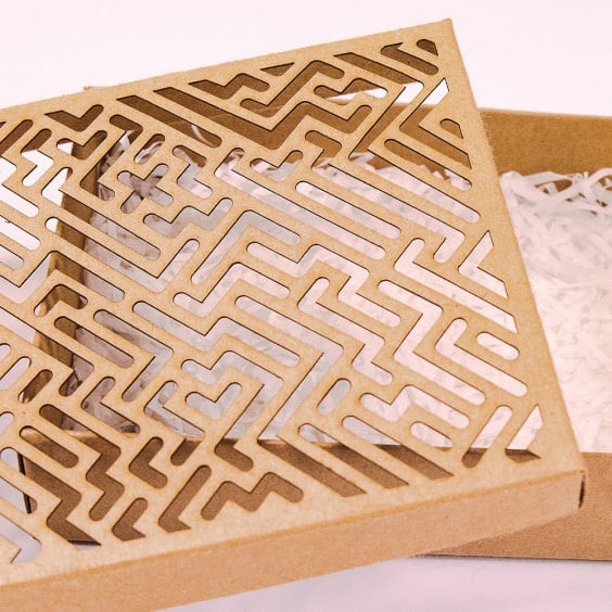 Cardboard box with an intricate geometric pattern laser-cut into the lid using the FLUX Beamo, partially open with shredded paper inside.