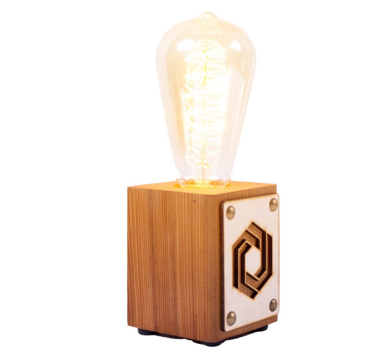 Glowing lightbulb on a wooden base with a laser cut FLUX logo on a wooden square fixed to the side.