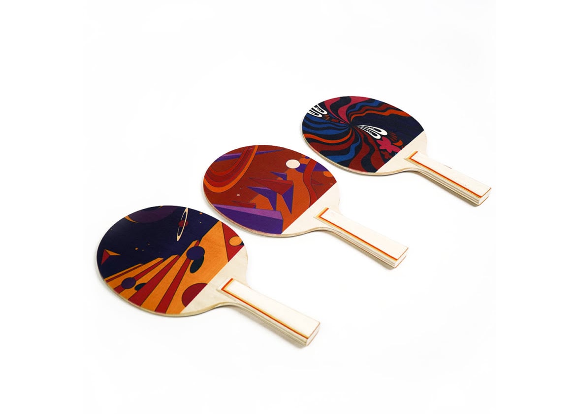 Three wooden table tennis bats at an angle with colorful printed geometric shapes.