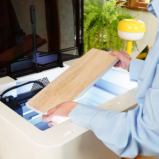 A woman placing a light piece of wood in a FLUX Ador with an open lid.