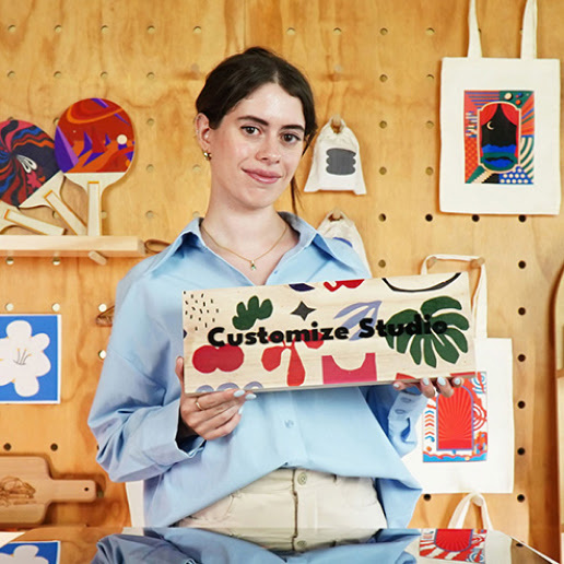 A woman showing a piece of wood with printed colorful shapes and the words 'Customize Studio' in black