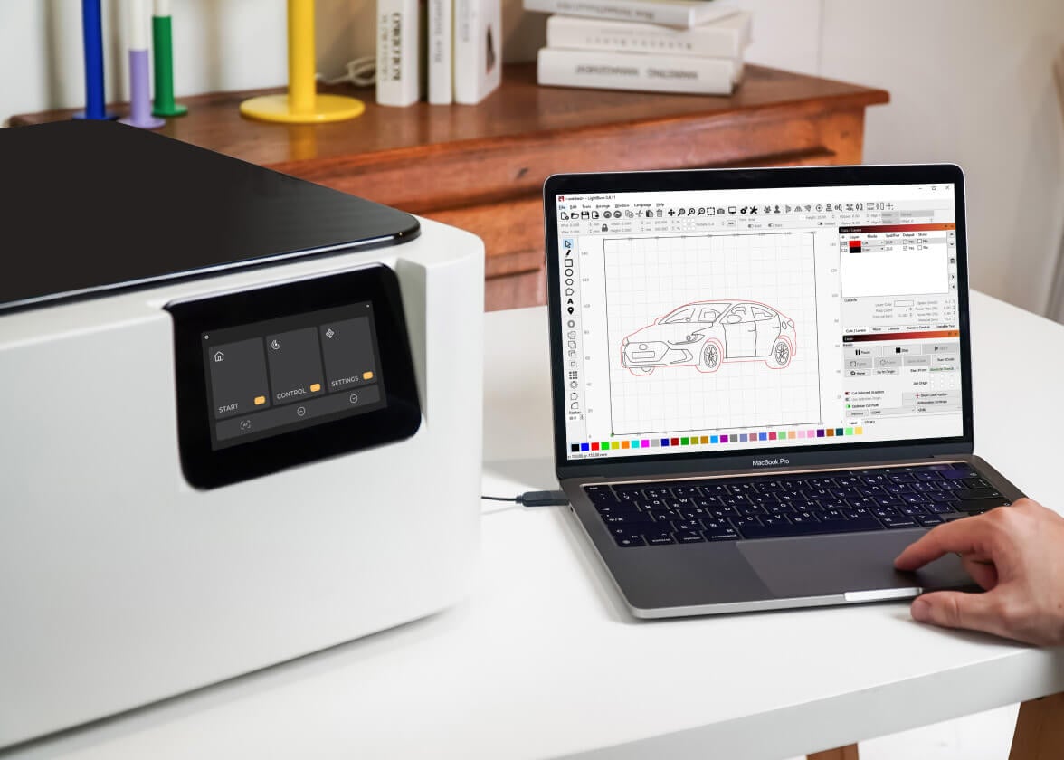 Laptop showing LightBurn software next to a FLUX Ador on a white table.