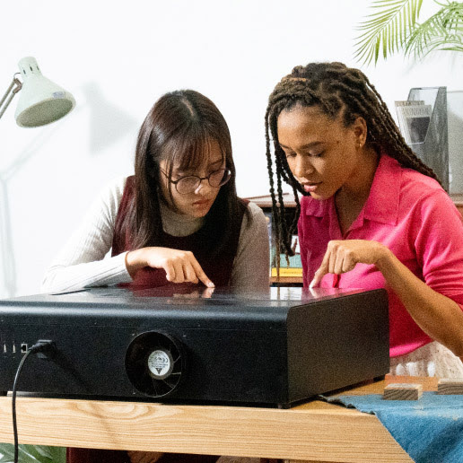 Two girls looking at their design being cut by a FLUX Beamo and pointing at it.