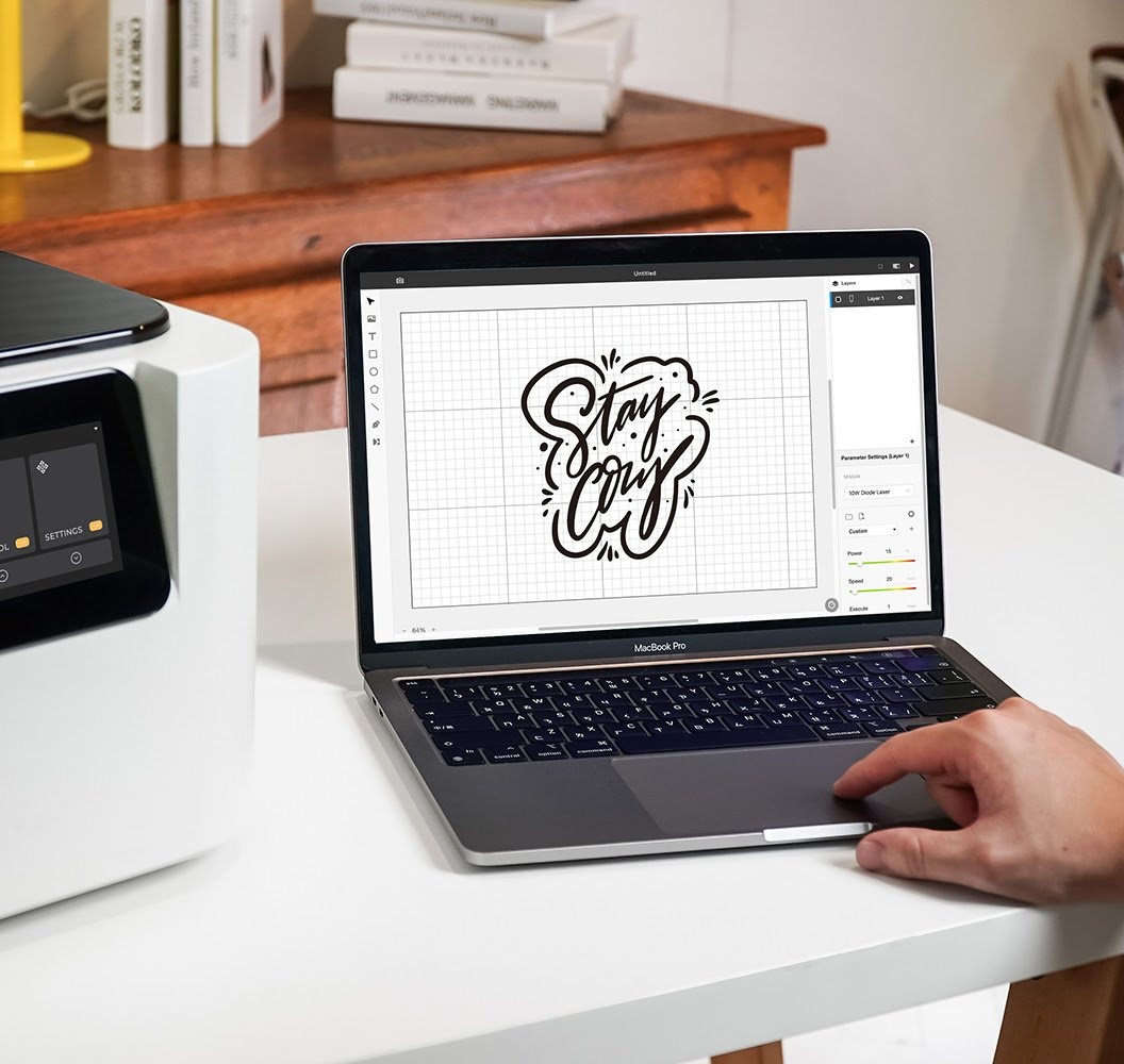 A laptop next to a FLUX Ador with FLUX Beam Studio open on a design that reads 'Stay Cozy'.