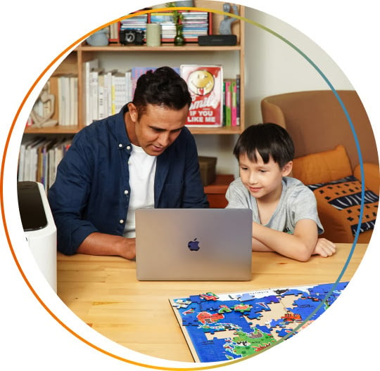 A man and a young boy working on a laptop next to a FLUX Ador. In front of them is a laser cut and printed jigsaw puzzle of a world map.