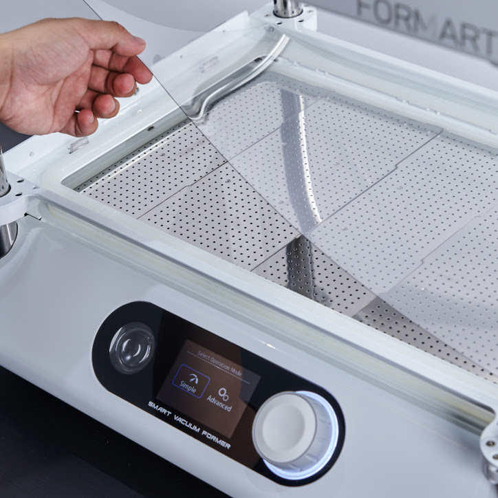A hand is putting a clear PET sheet into the vacuum former.