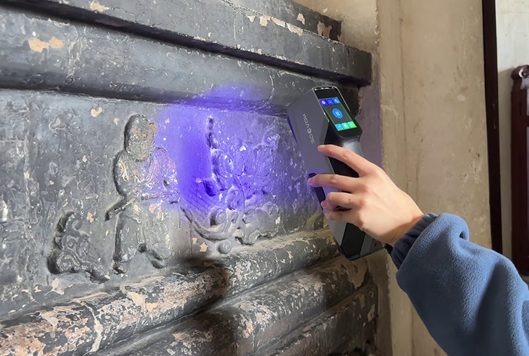 Hand holding a 3DeVOK 3D scanner scanning ancient wall carvings 