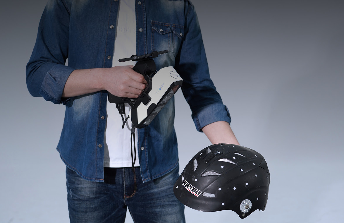 Man 3D scanning a black bicycle helmet with markers with the 3DeVOK MQ and the optional wireless handle.