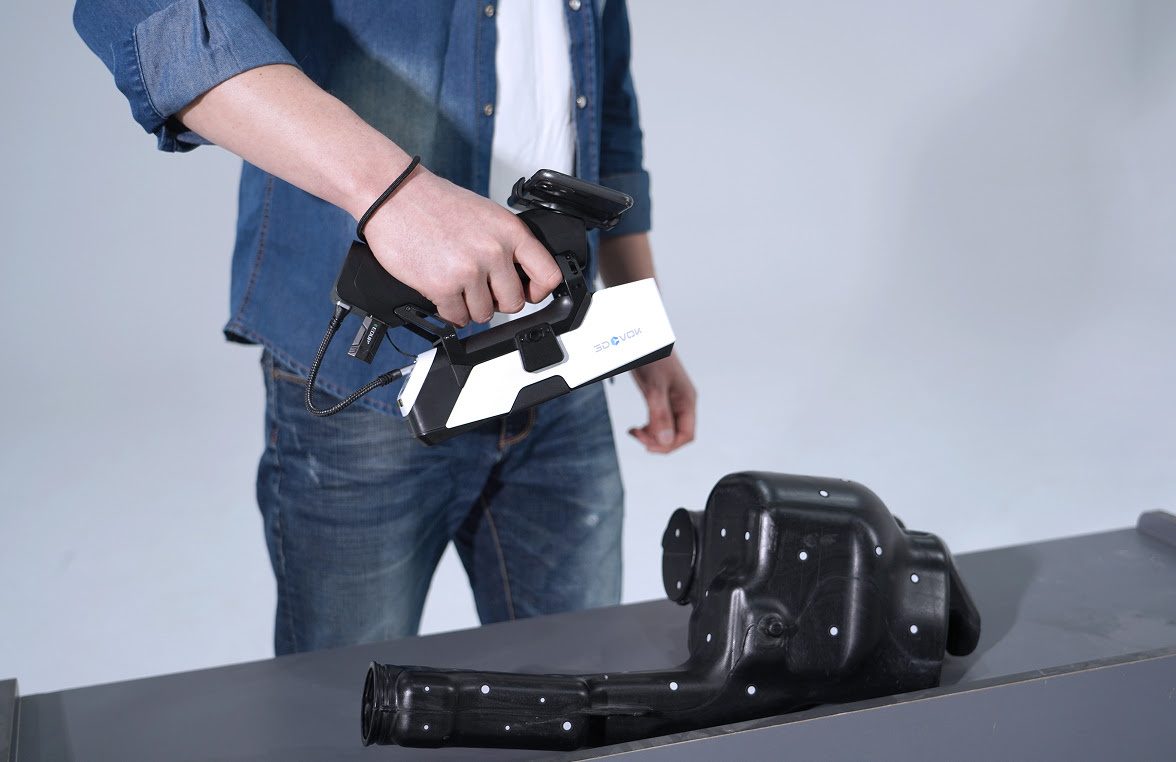 Man holding the 3DeVOK MQ with the optional wireless handle and scanning a black objects with markers on a table.
