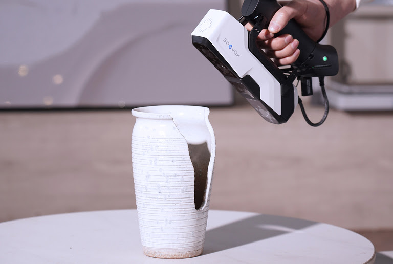 Hand holding the 3DeVOK MQ 3D scanner and 3D scanning a vase with a large piece of it missing.