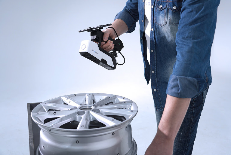 Man holding the 3DeVOK MQ with the optional wireless handle and scanning a car rim.
