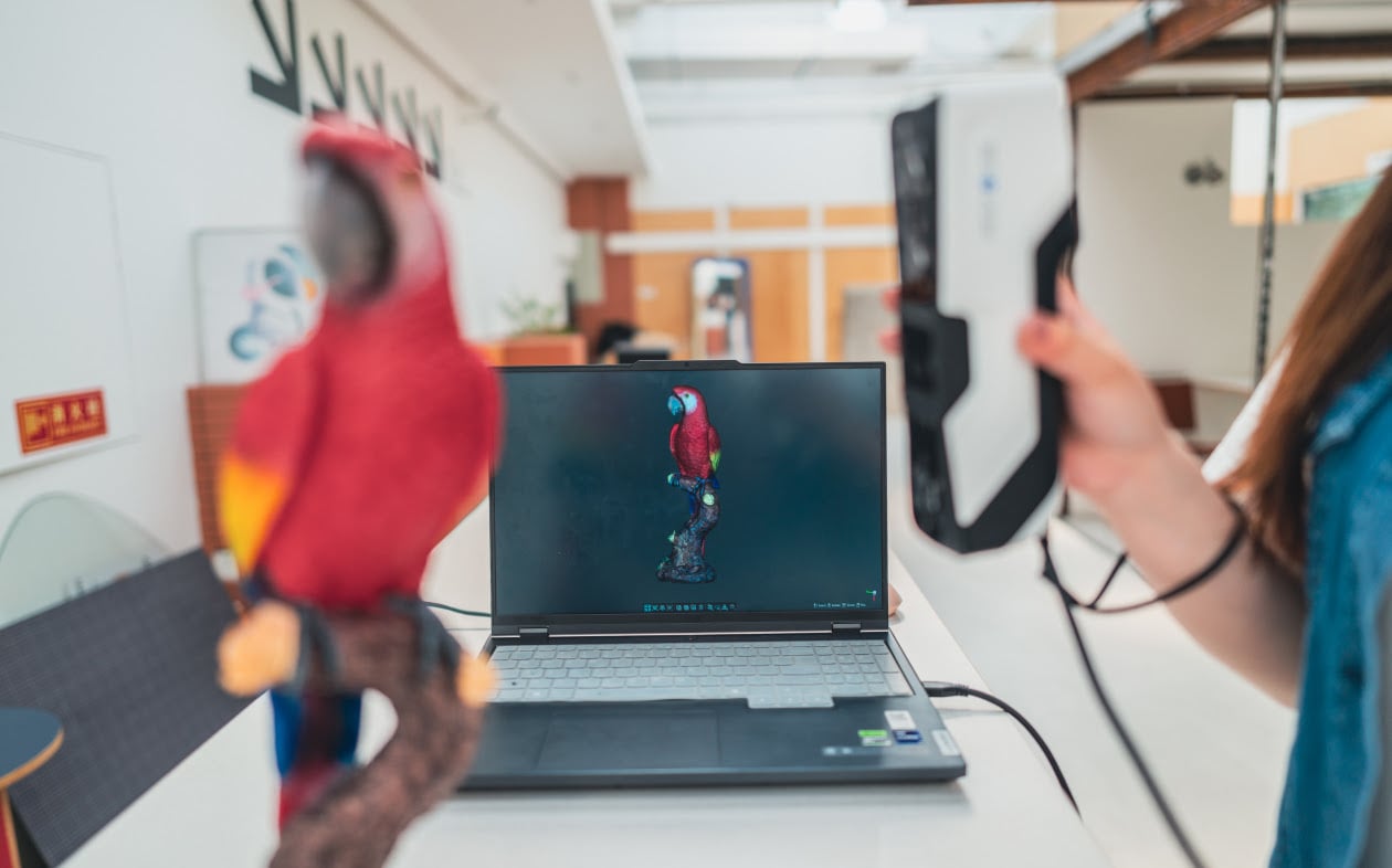 Colorful parrot statue being scanned with a 3DeVOK MQ. A laptop with a live view of the parrot 3D scan is in the  background.
