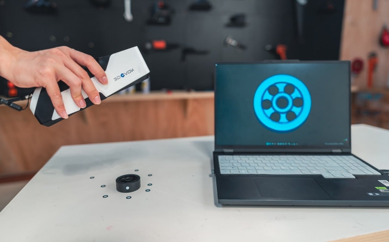 Hand holding a 3DeVOK MQ and scanning a small cylindrical object. Next to it there is a laptop showing the live 3D scan view