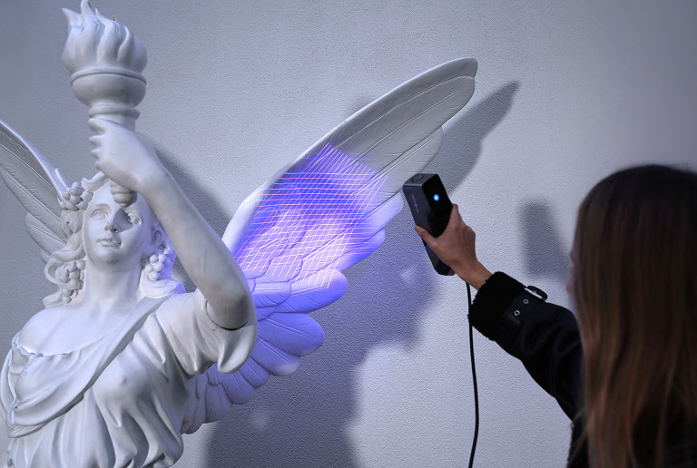 Woman holding the 3DeVOK MT and scanning the wing of an angle statue with the 34 blue laser line mode.